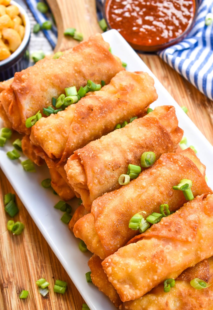macaroni and cheese egg rolls on a white platter topped with sliced green onions