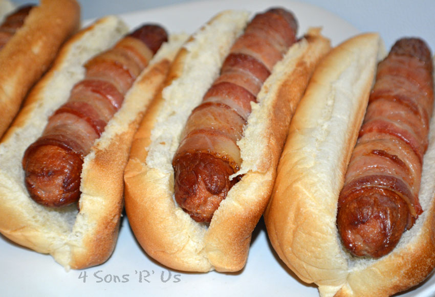 baked bacon wrapped hot dogs in plain white buns arranged in a row