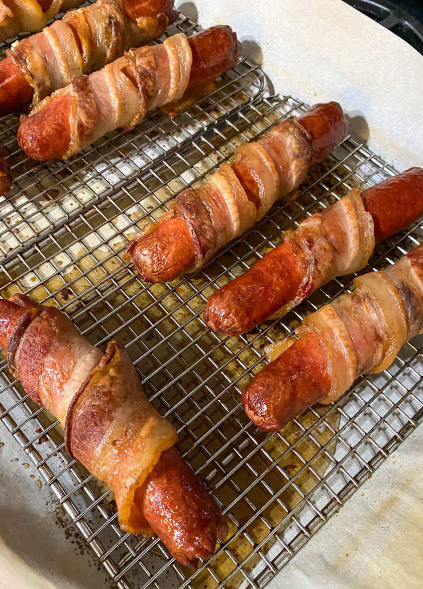 baked bacon wrapped hot dogs on wire racks on top of a parchment paper lined baking sheet