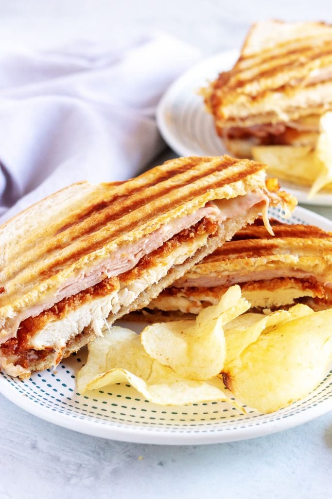 Chicken Cordon Bleu Paninis are halved and shown on white plates with potato chips on the side