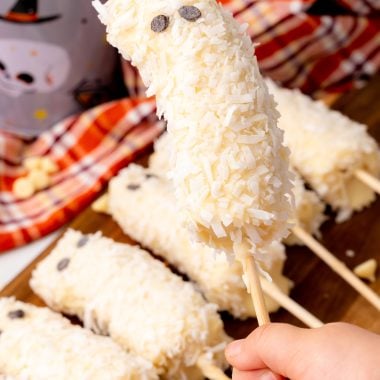 a little hand holding up a coconut and white chocolate crusted boo-nana ghost popsicle