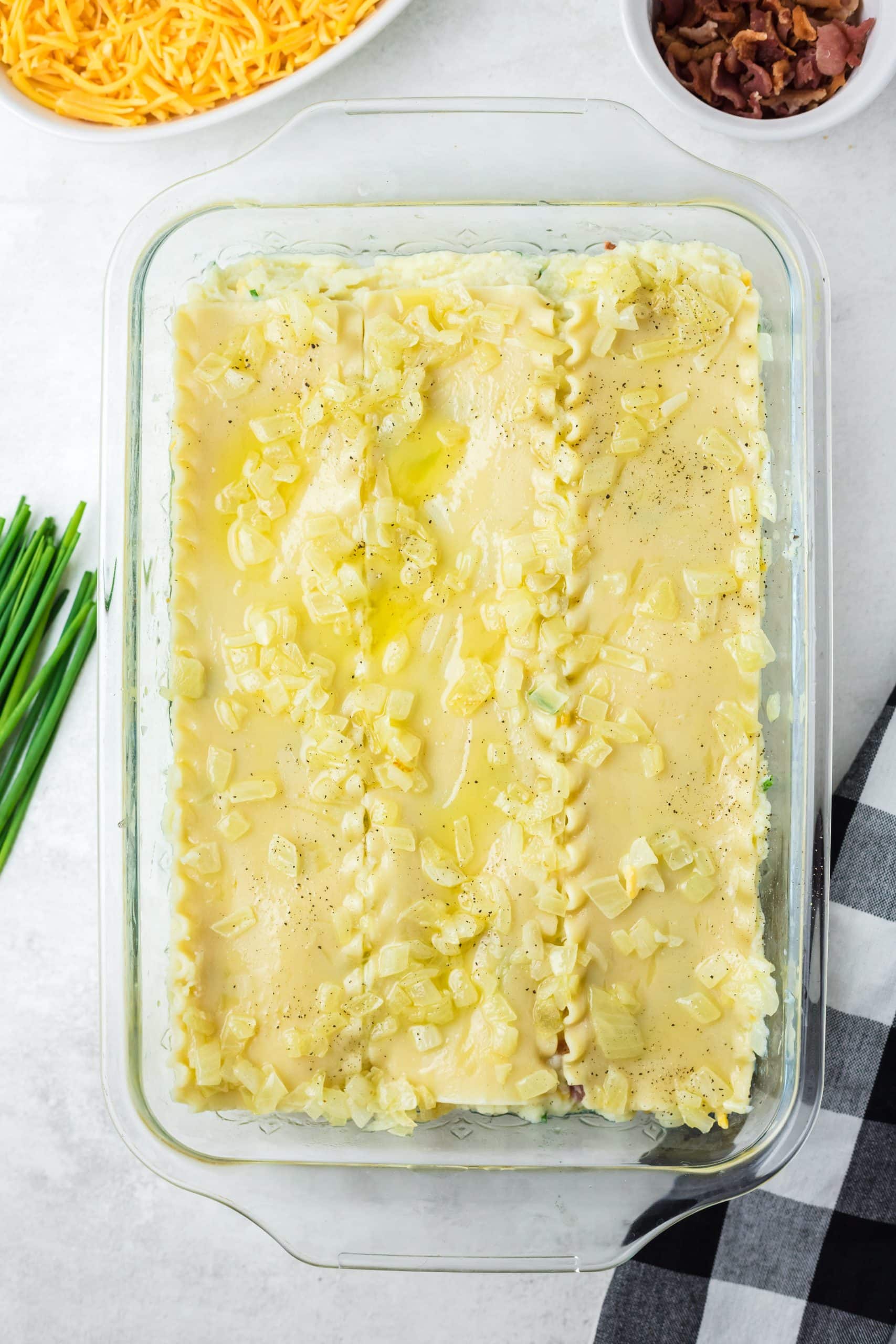 sauteed onions and butter spread out over a layer of lasagna noodles in a glass baking dish