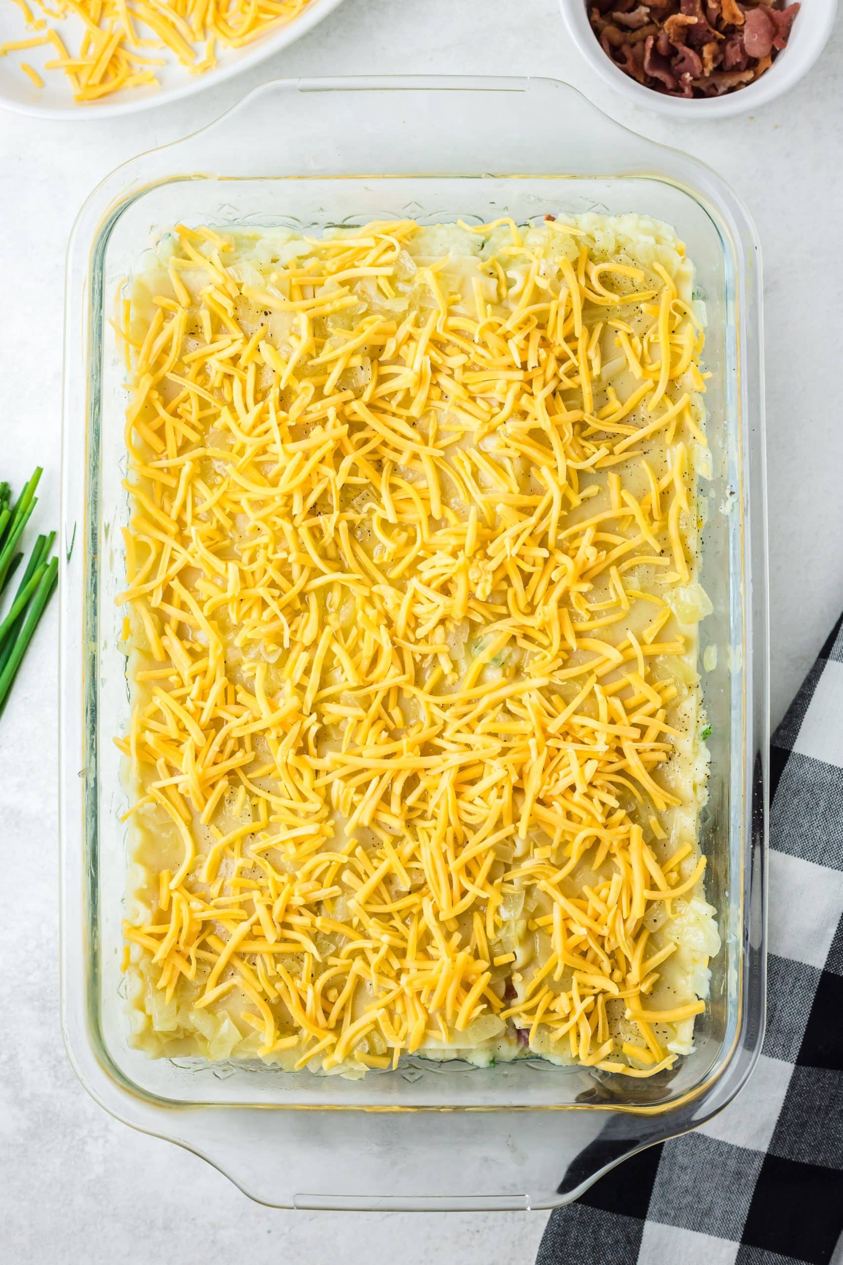 shredded cheddar spread out over the top layer of a pierogi lasagna in a glass baking dish
