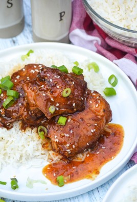 crockpot honey garlic chicken thighs & sauce spread over steamed white rice on a white plate