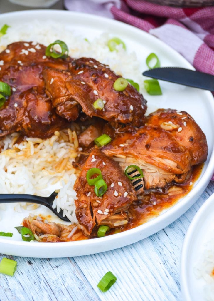 a black fork topped with white rice and honey garlic chicken resting on a white plate