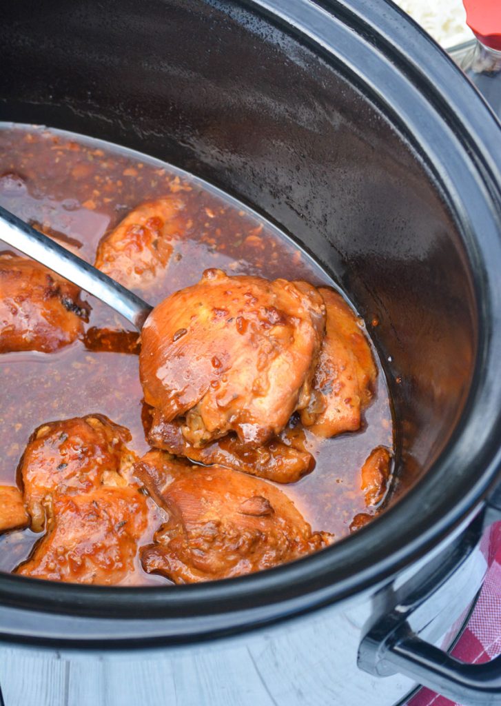 a silver spoon shown lifting honey garlic chicken out of a black crockpot