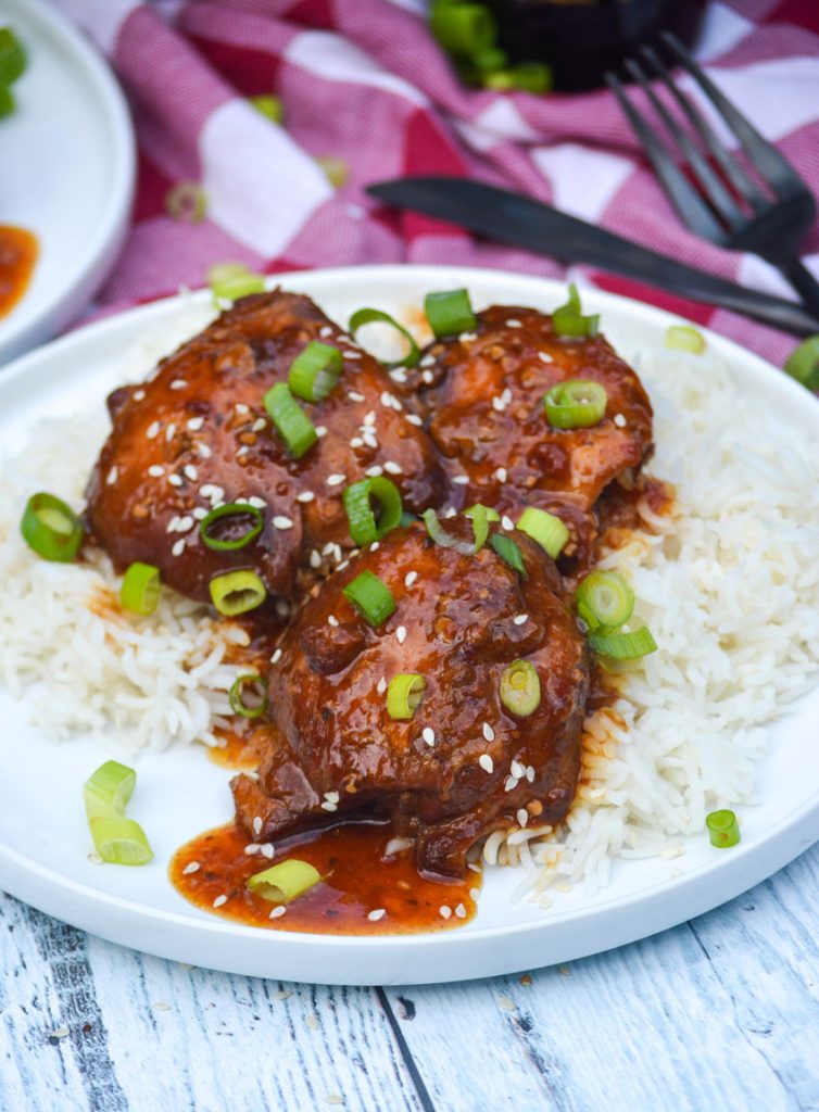 crockpot honey garlic chicken thighs & sauce spread over steamed white rice on a white plate