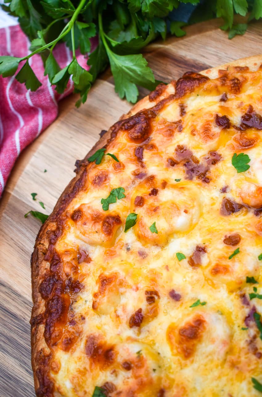 garlic shrimp alfredo pizza on a wooden pizza peel with fresh herbs in the background