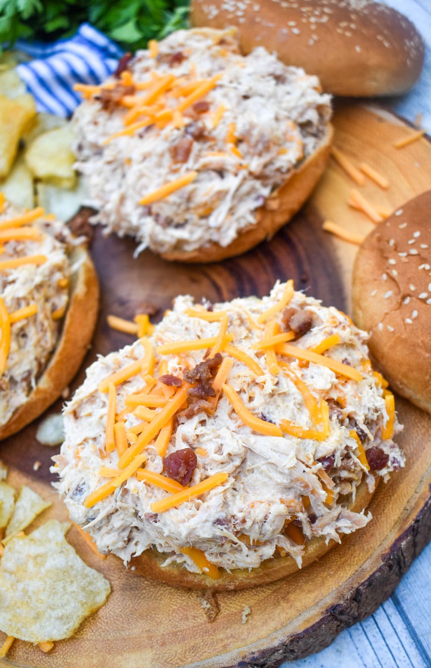 crockpot crack chicken sandwiches next to potato chips on a wooden cutting board