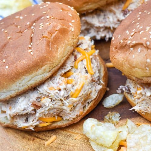 slow cooker crack chicken sandwiches next to potato chips on a wooden cutting board