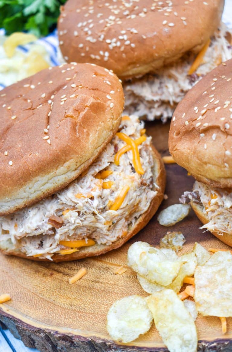 slow cooker crack chicken sandwiches next to potato chips on a wooden cutting board