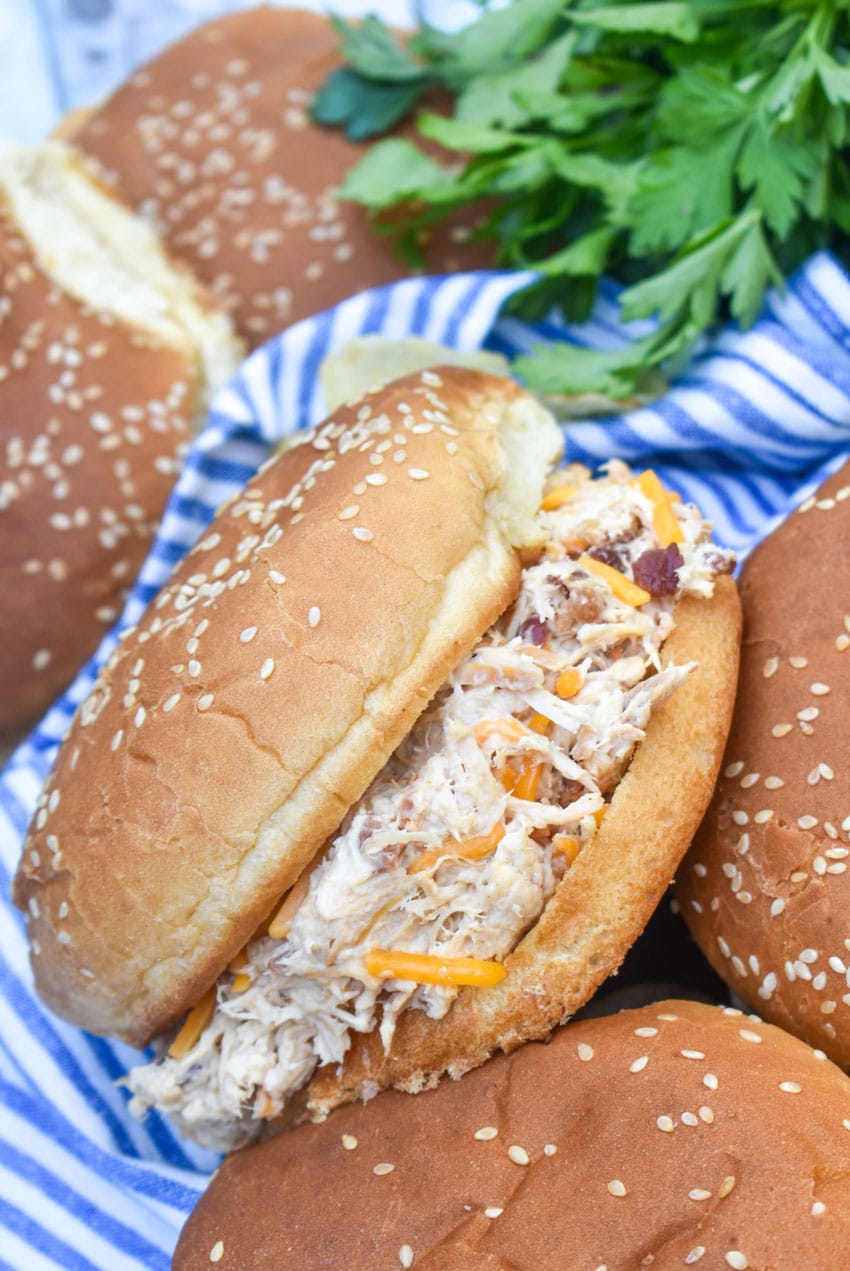 crockpot crack chicken sandwiches next to potato chips on a wooden cutting board