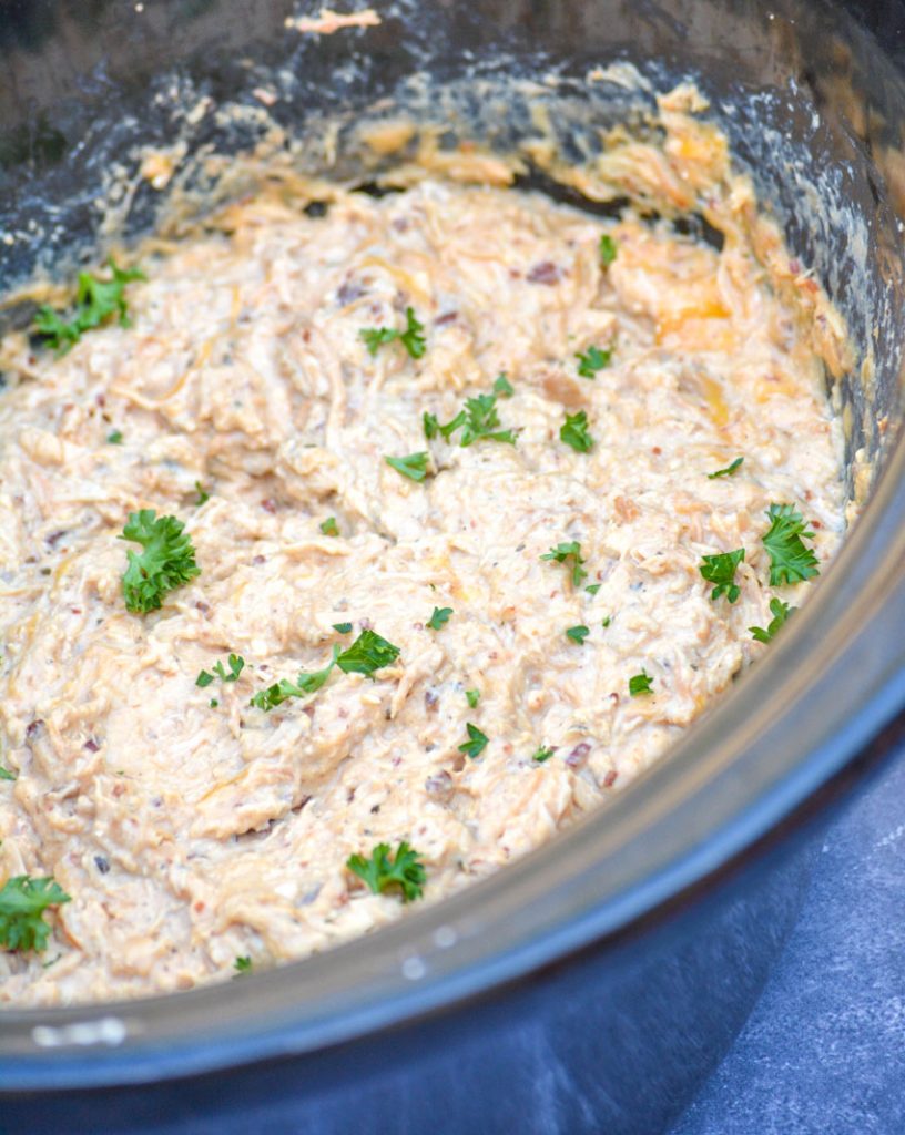 crockpot crack chicken in the bowl of a black crockpot sprinkled with fresh parsley leaves