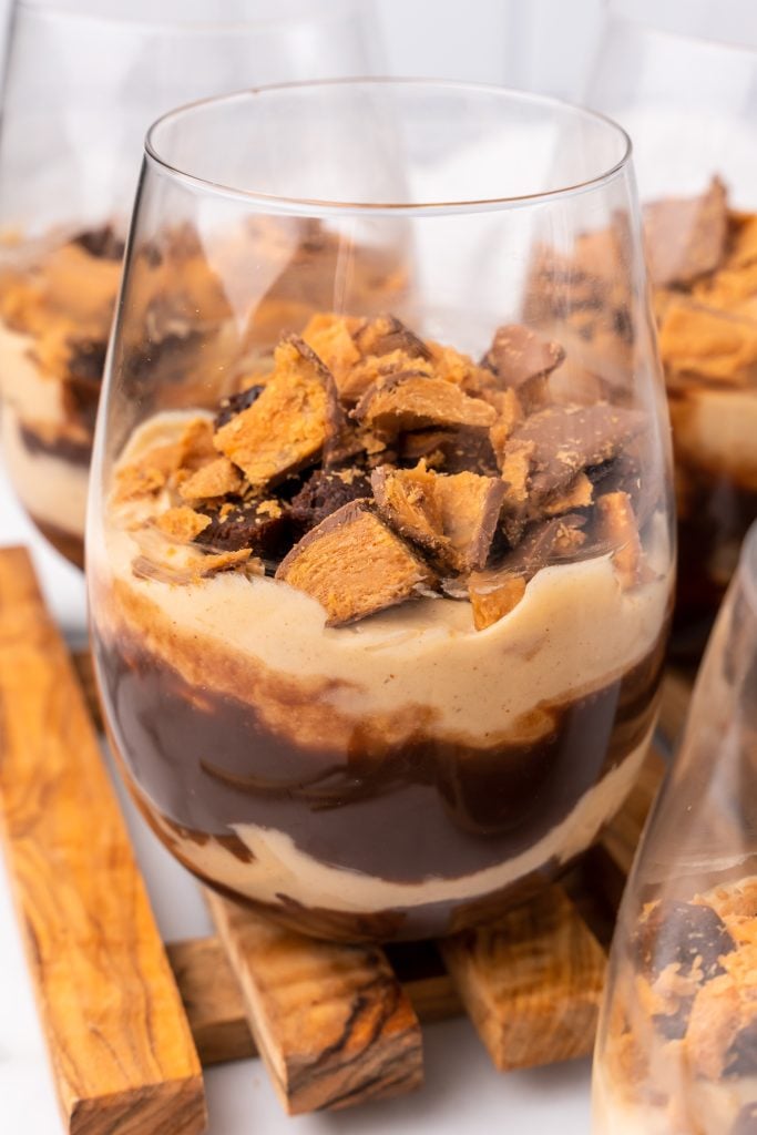 a layered butterfinger trifle on a stemless wine glass on a wooden cutting board