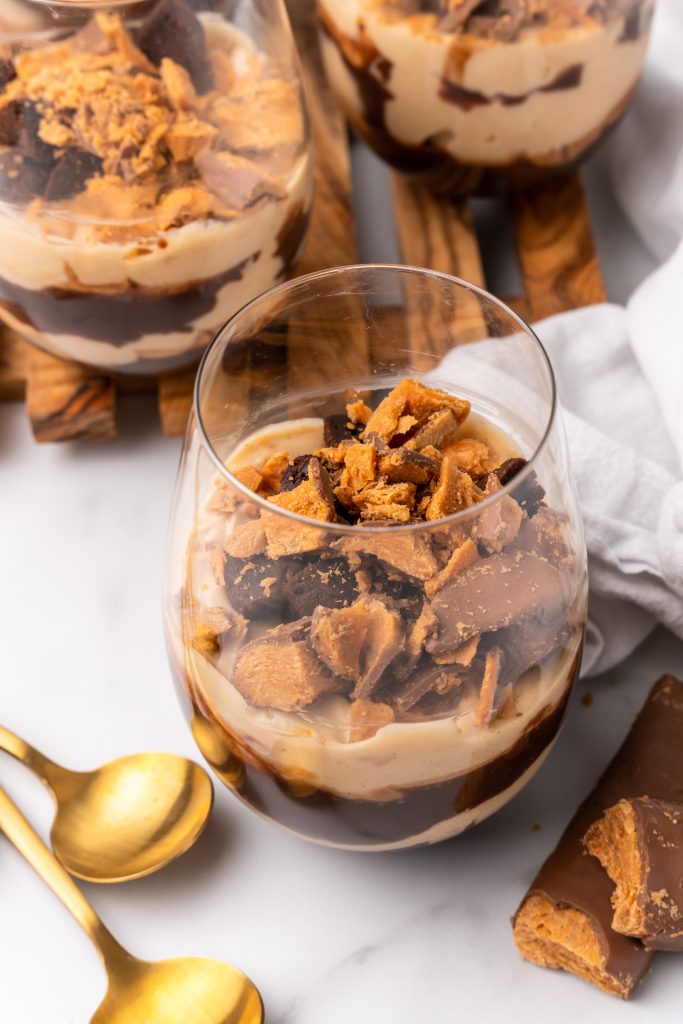 a layered butterfinger trifle on a stemless wine glass on a wooden cutting board