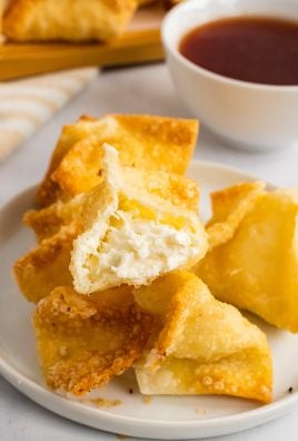 an opened crab rangoon on top of a pile of crab rangoon showing the creamy cheese filling inside