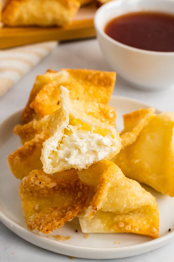 an opened crab rangoon on top of a pile of crab rangoon showing the creamy cheese filling inside