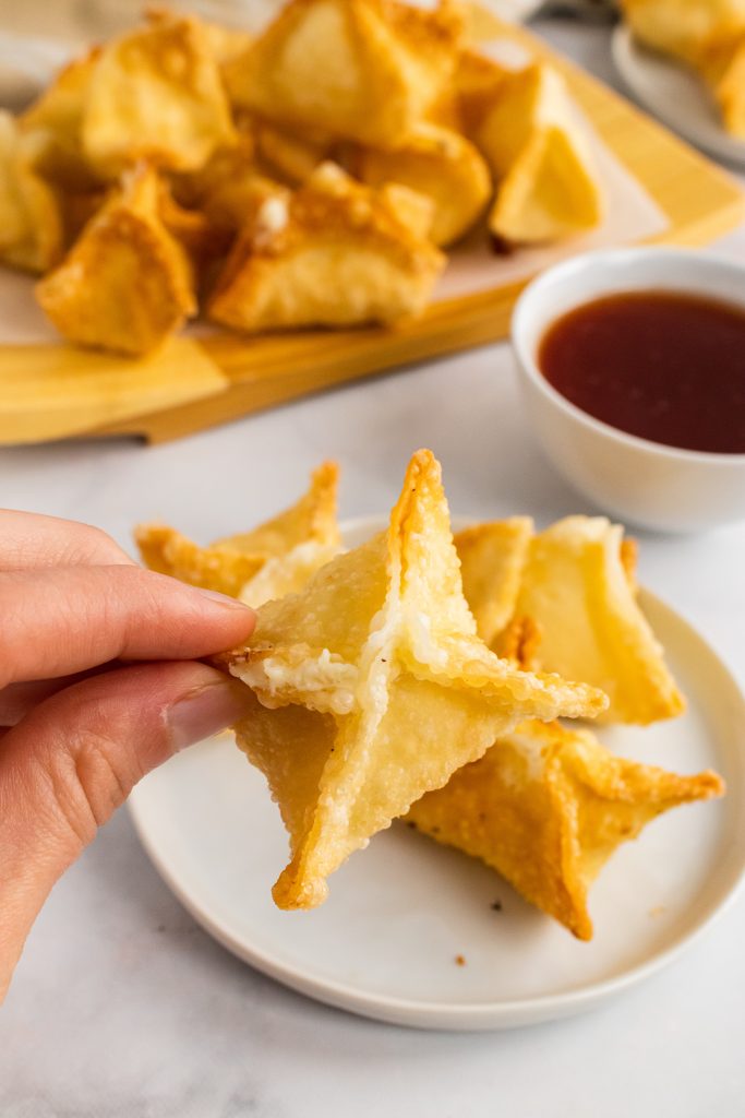 a hand holding up a golden brown fried crab rangoon