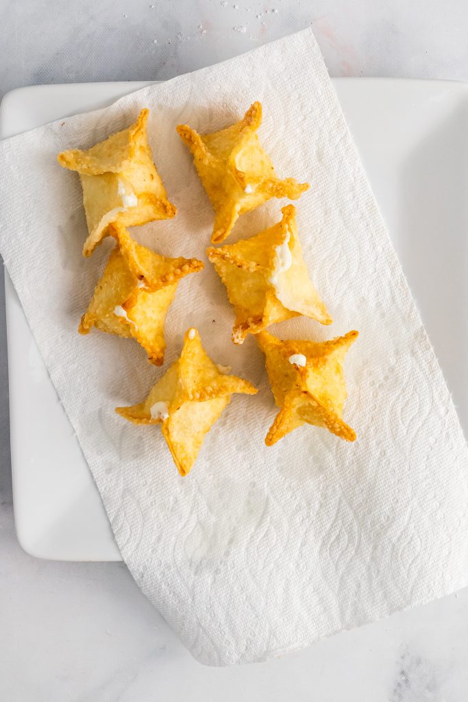 fried crab rangoon arranged on a paper towel lined white plate