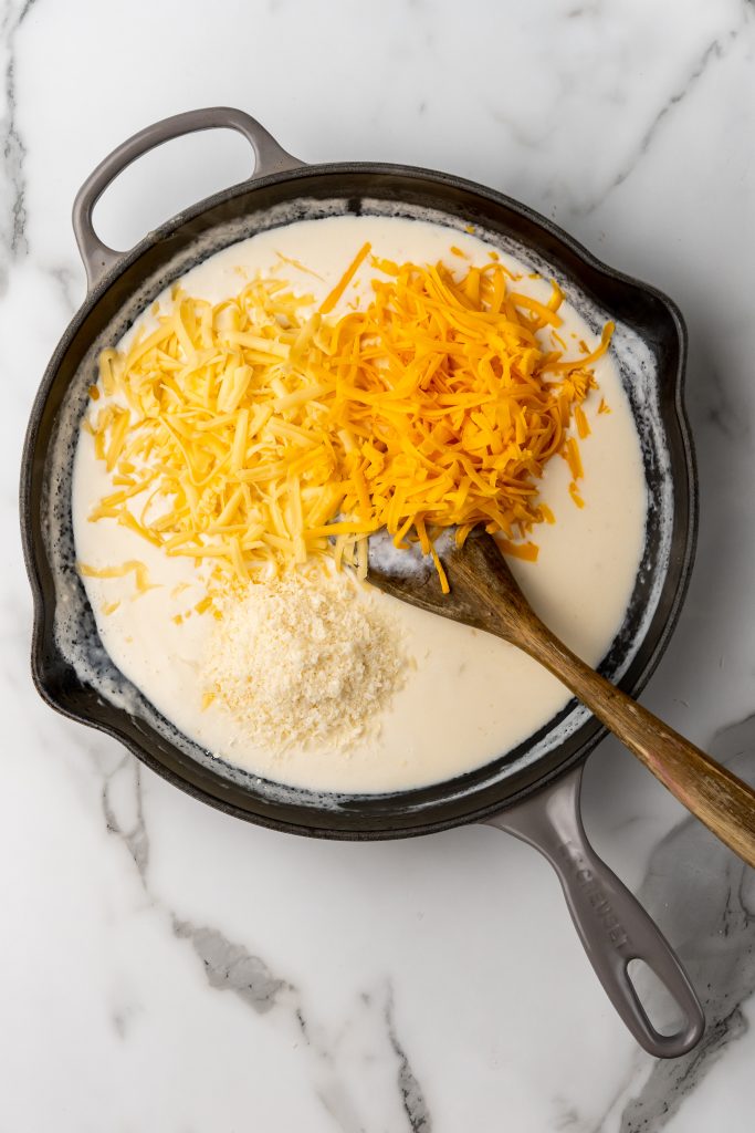 three different shredded cheeses in a cast iron skillet with a cream sauce