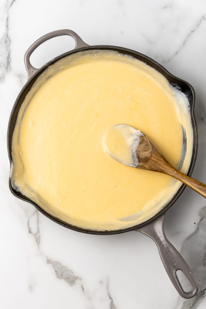 a creamy homemade cheese sauce in a cast iron skillet with a wooden spoon stuck in the middle