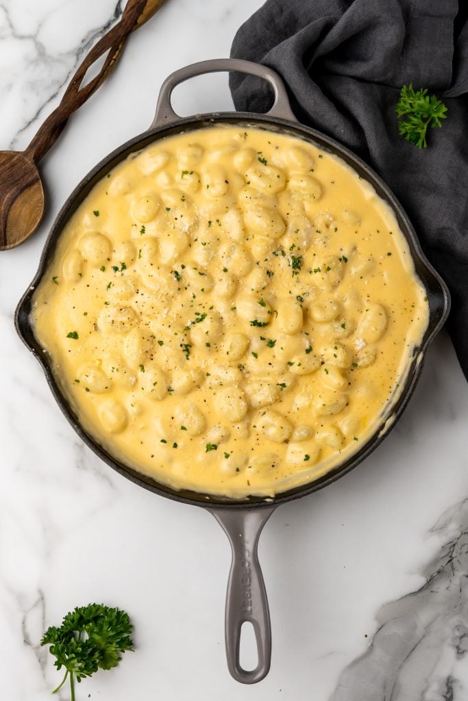 three cheese gnocchi mac and cheese in a cast iron skillet with a wooden spoon on the side