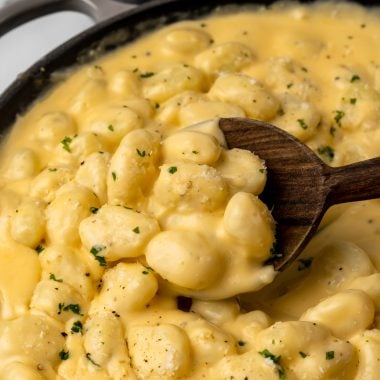 a wooden spoon scooping three cheese gnocchi mac and cheese out of a black skillet