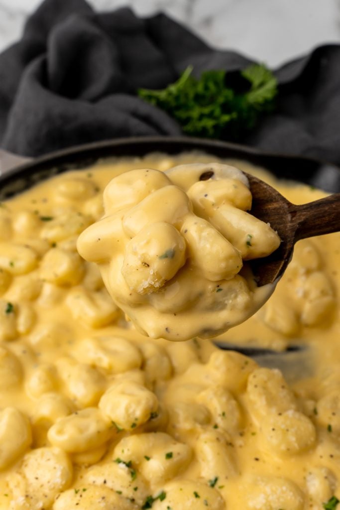 a wooden spoon holding up a scoop of extra creamy three cheese gnocchi mac