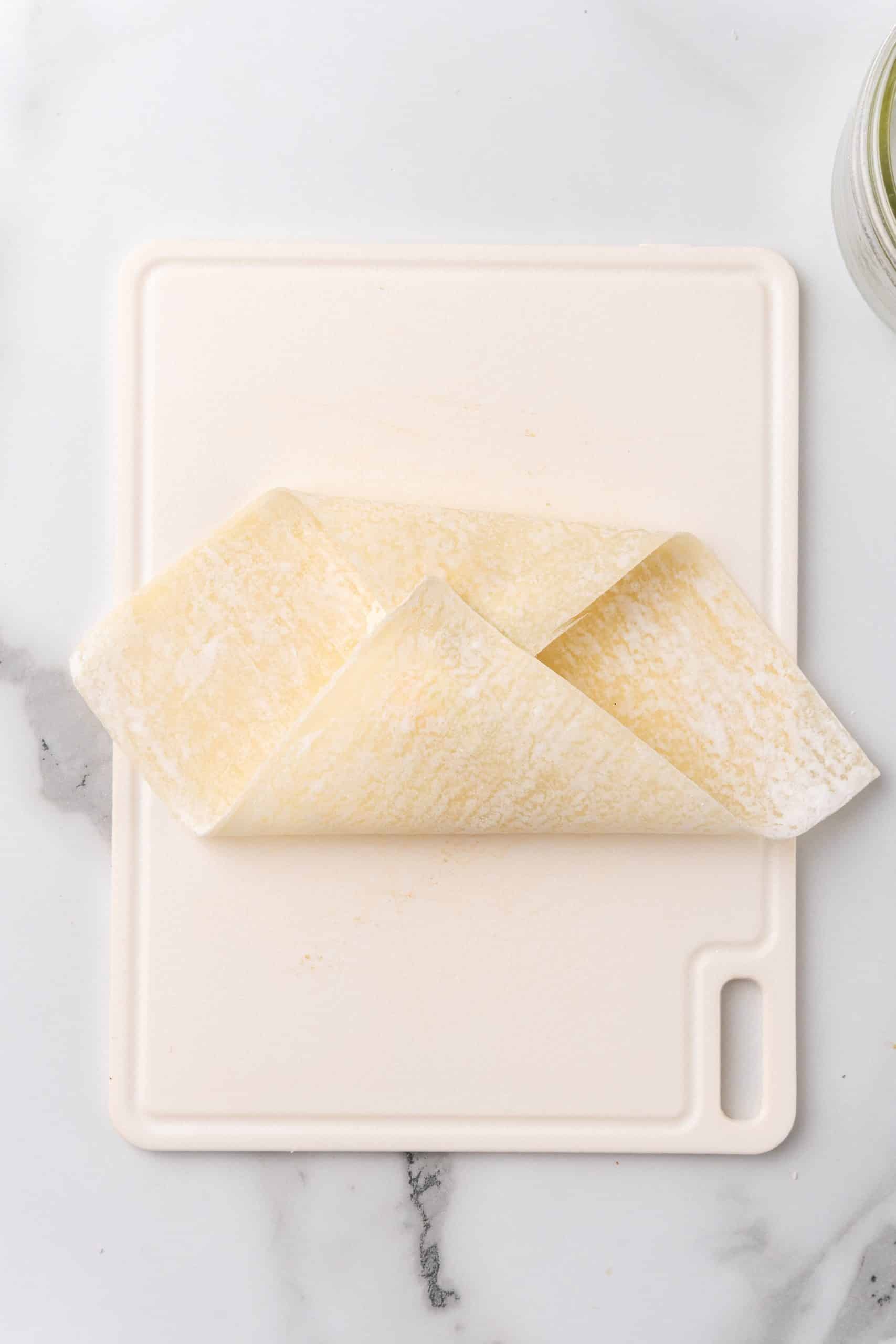 a wonton wrapper folded in half over cream cheese filling on a white cutting board