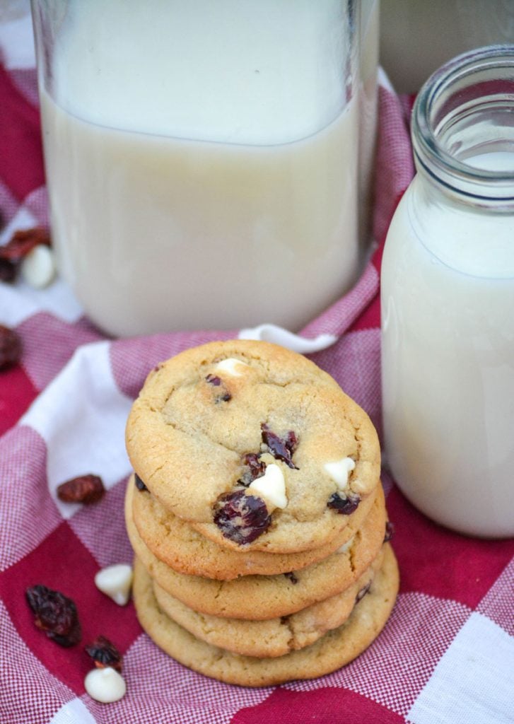 a stack of chewy white chocolate chip & cranberry cookies beside a glass of cold milk
