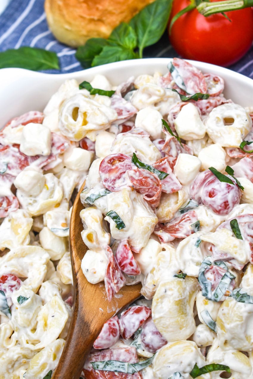 a wooden spoon scooping creamy tortellini pasta salad out of a white serving bowl