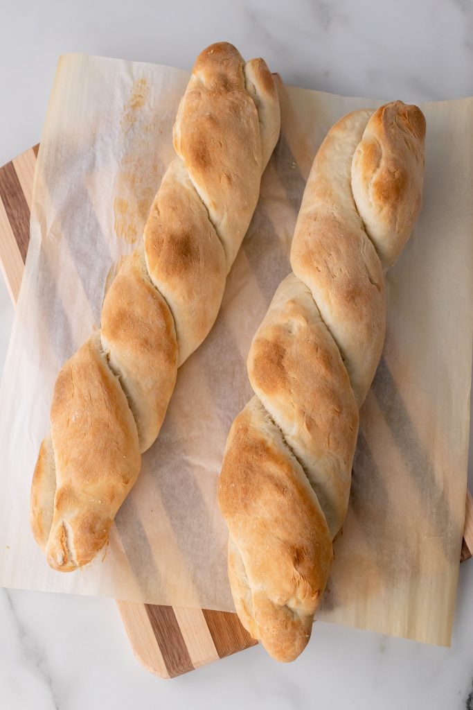 two baked foolproof baguettes on a parchment paper covered wooden cutting board