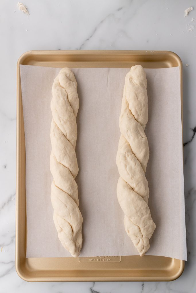 two twisted unbaked loaves of french baguettes on a parchment paper covered baking pan