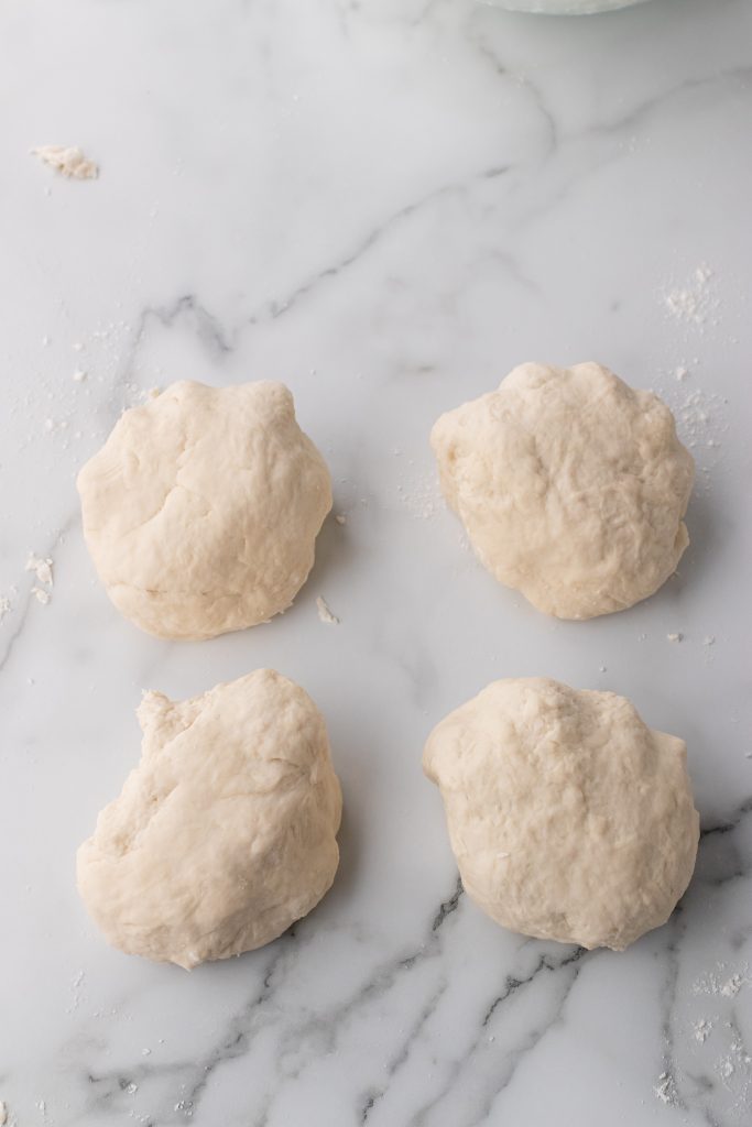 four small balls of fool proof baguette dough on a marbled countertop