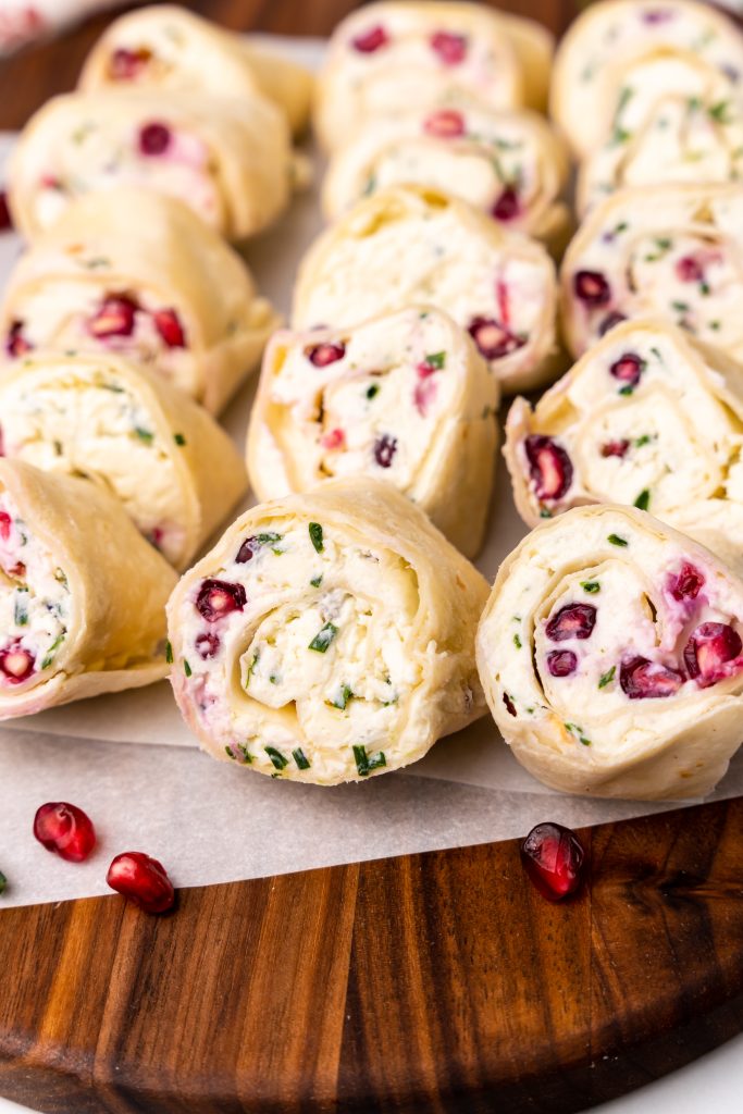 pomegranate feta and chive pinwheels on a wooden cutting board with arils and fresh chives