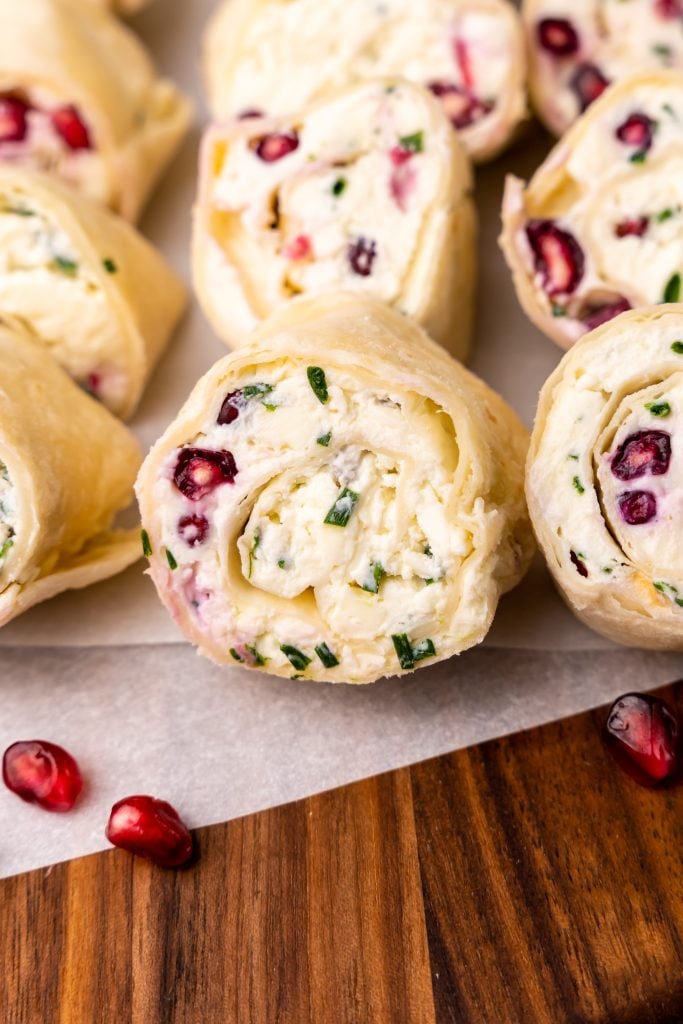 pomegranate feta and chive pinwheels on a wooden cutting board with arils and fresh chives