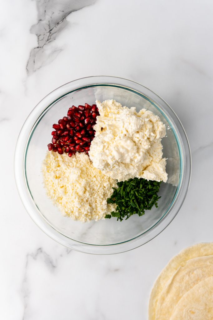 cream cheese, feta cheese, chopped chives, and pomegranate arils in a glass mixing bowl