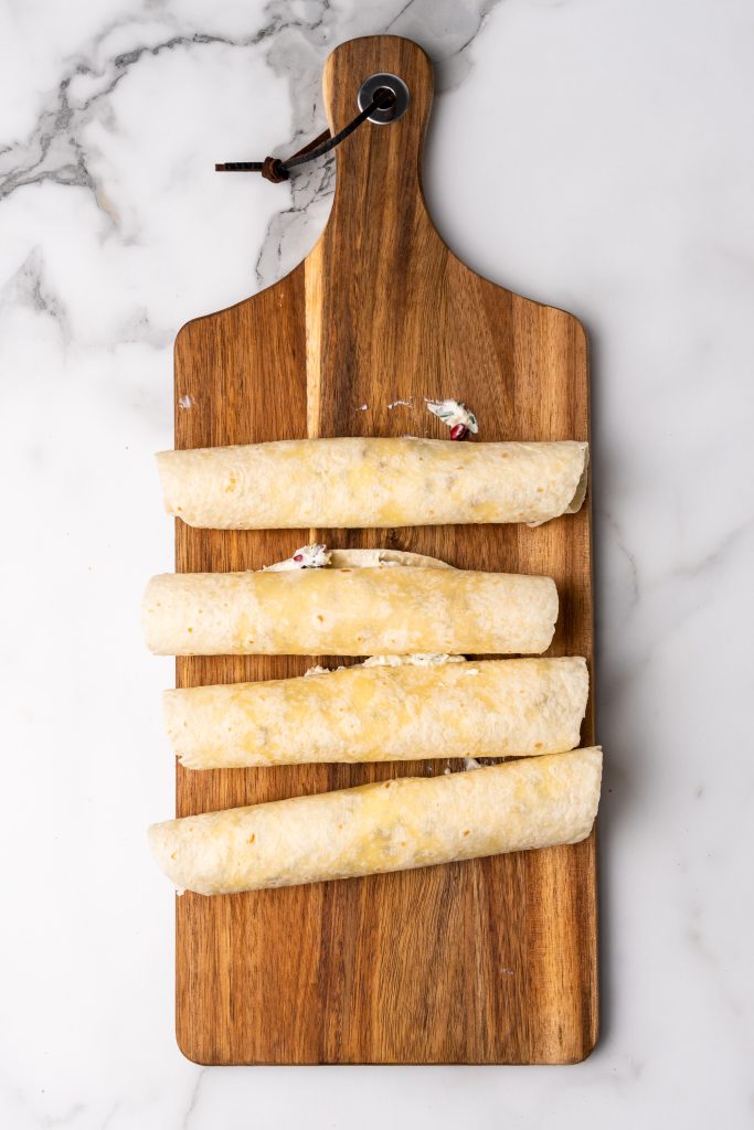 rolled tortillas filled a holiday cream cheese mixture on a wooden cutting board