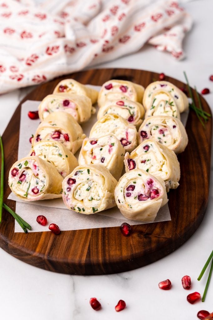 pomegranate feta and chive pinwheels arranged in three rows on a wooden cutting board