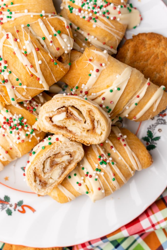 white chocolate gingerbread crescent rolls piled on a white serving platter with one cut in half to show the center layers