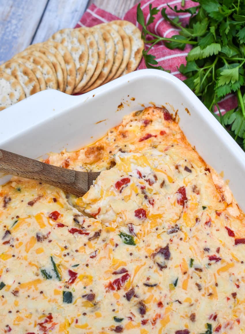 a wooden spoon scooping hot pimento cheese dip out of a white baking dish