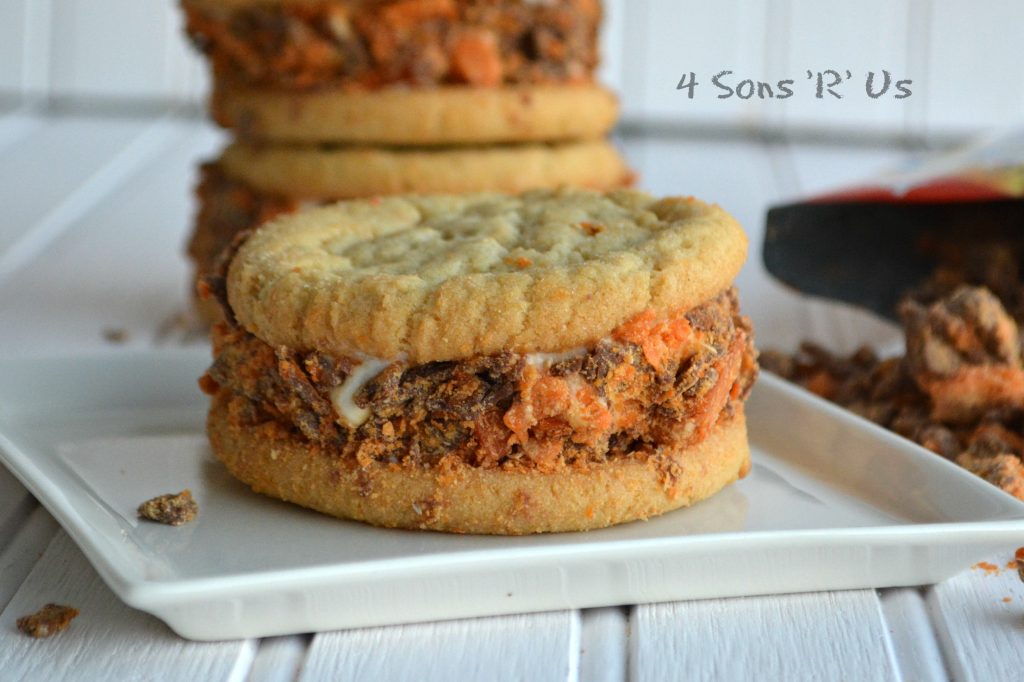 a single Butterfinger Sugar Cookie Ice Cream Sandwich shown on a small white appetizer plate with butterfinger candy pieces in the background