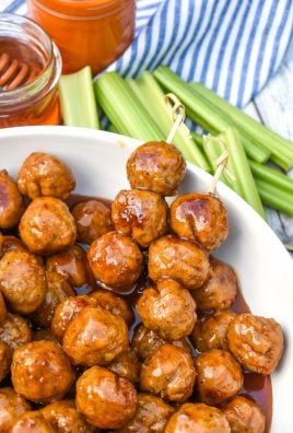 two toothpicks skewered with slow cooker honey buffalo meatballs resting on the edge of a white bowl