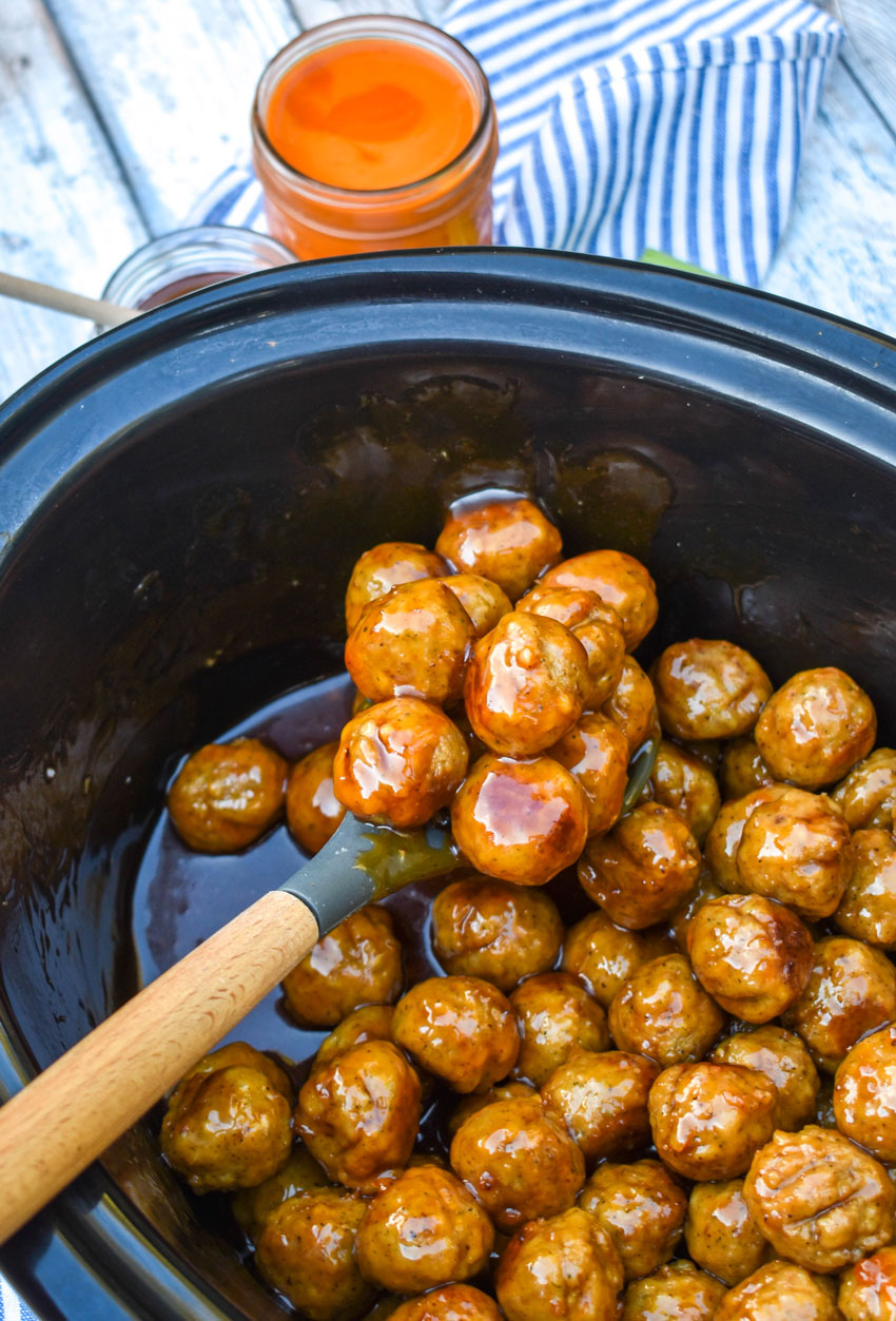 a spoon in a black crockpot filled with honey & buffalo sauce coated meatballs