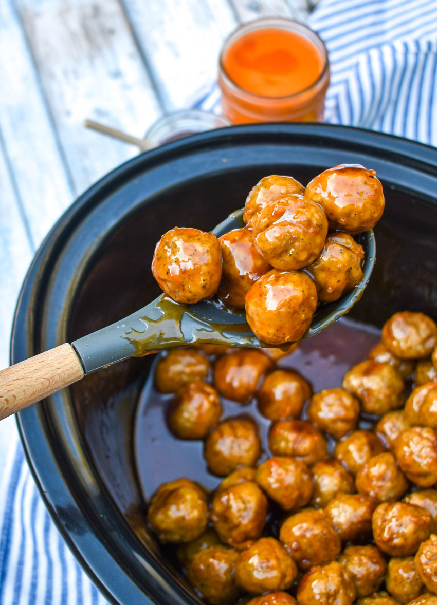 a wooden handled spoon holding a scoop of crockpot honey buffalo meatballs up in the air