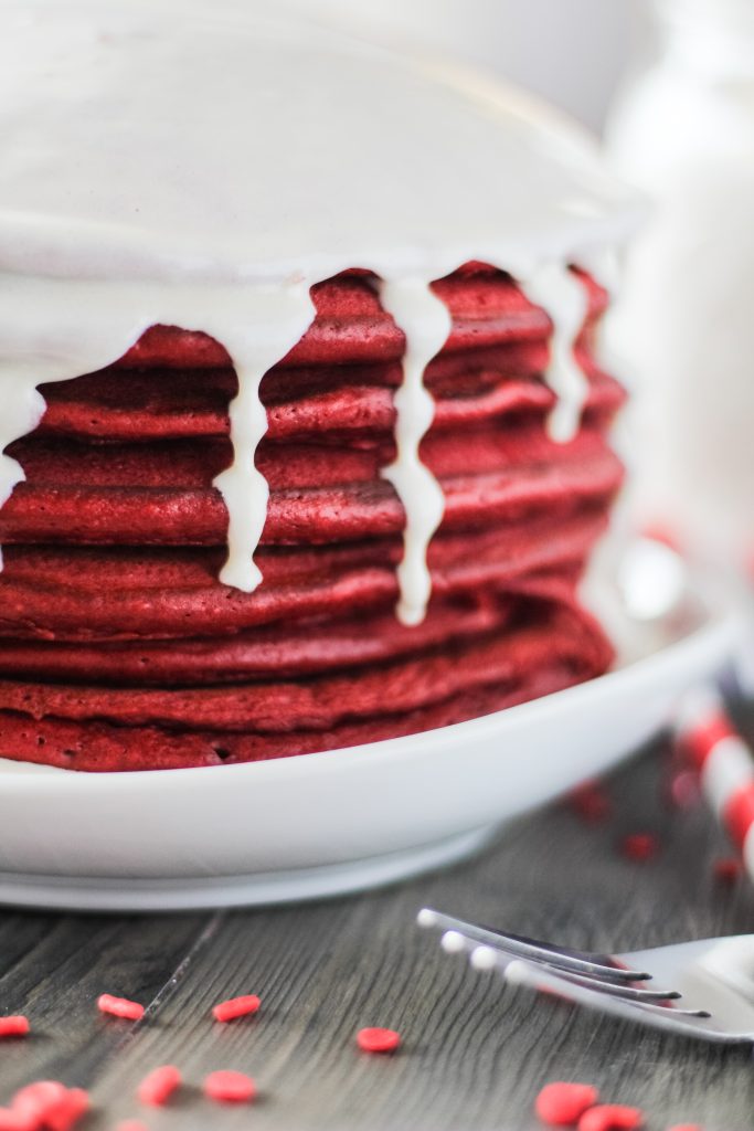 a stack of red velvet pancakes with cream cheese glaze on a white plate