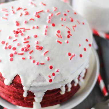 red velvet pancakes topped with cream cheese glaze stacked on a white plate