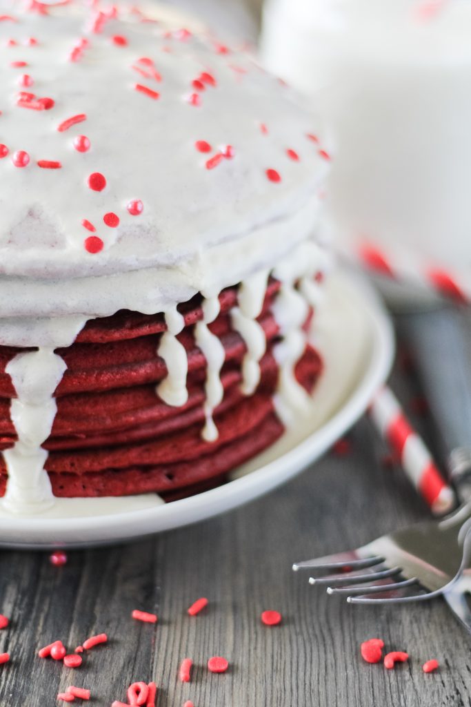 a stack of red velvet pancakes with cream cheese glaze on a white plate