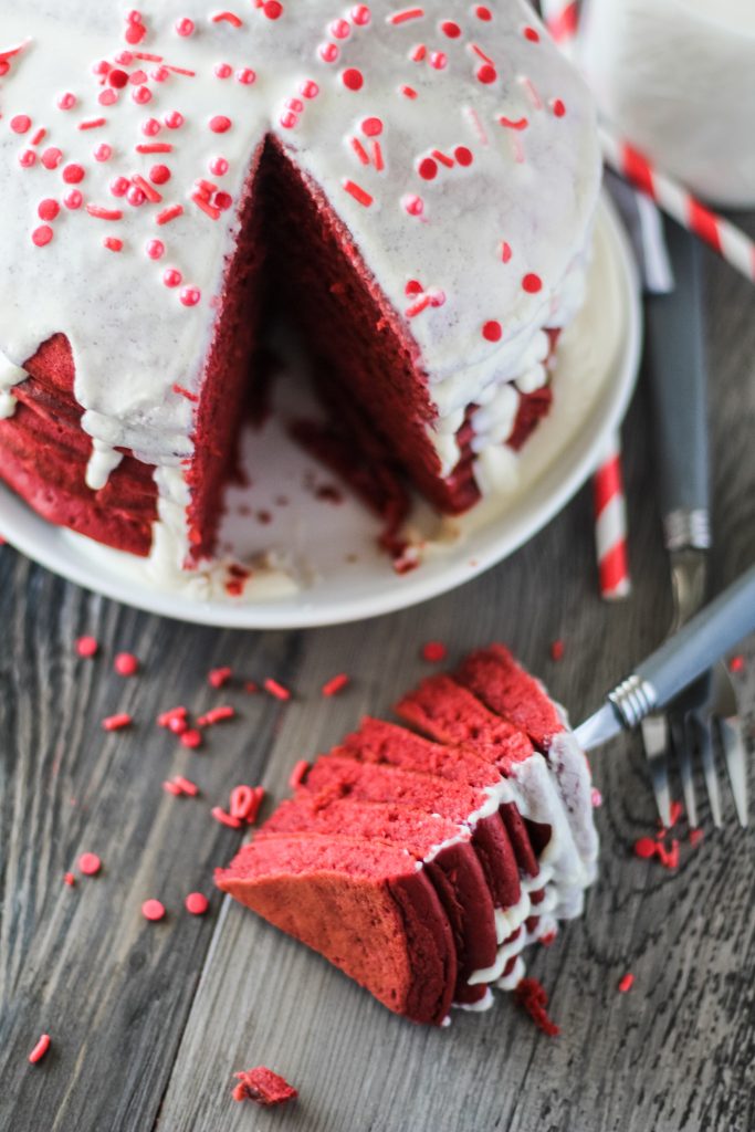 a stack of red velvet pancakes with cream cheese glaze on a white plate