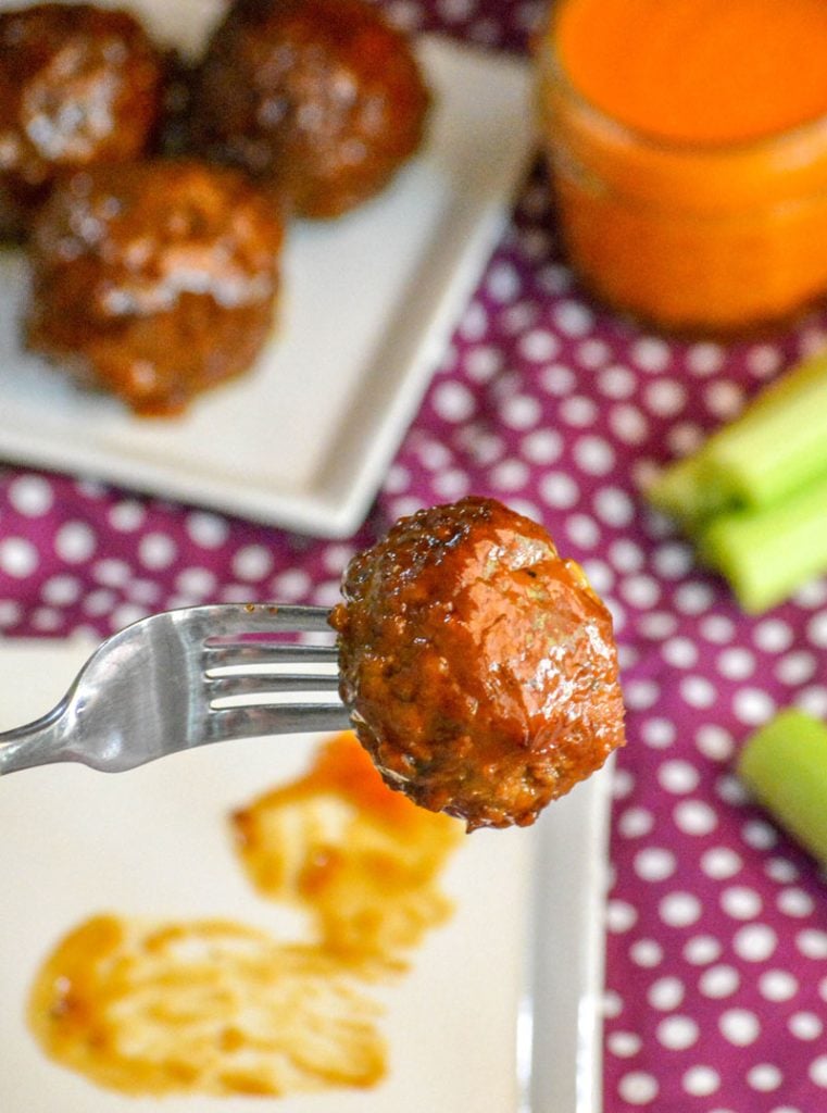 Slow Cooked Sweet & Spicy Saucy Meatball held aloft by a silver fork for a close up shot